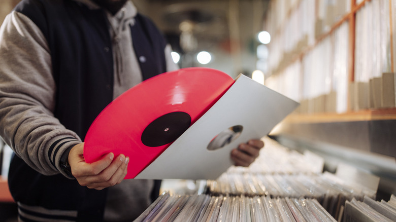 A man holds a red vinyl record while browsing in a record store