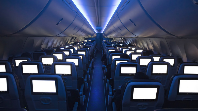 The interior of a passenger plane is shown with lights dimmed and all the TV screens blanked out