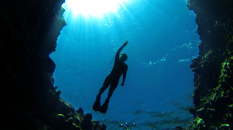 Silhouette of diver with arm raised towards water surface with rock walls on either side of him