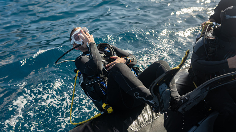 Male diver in scuba gear rolls backwards off boat into water