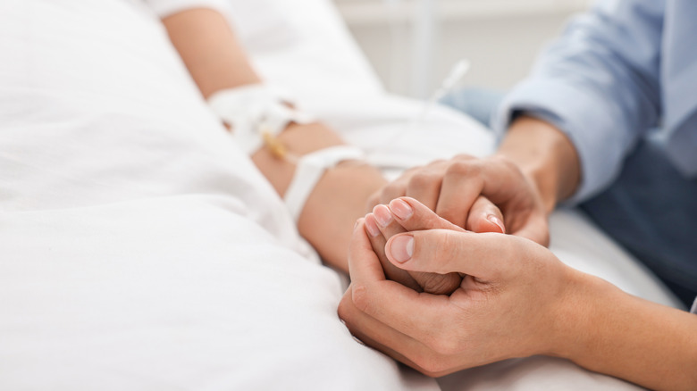 A hospital patient's hands are seen being held by the hands of a visitor