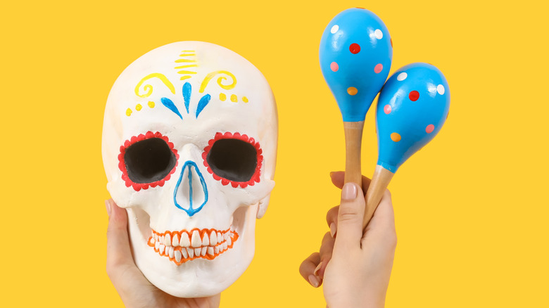 Female hands hold a skull and two maracas against a yellow background