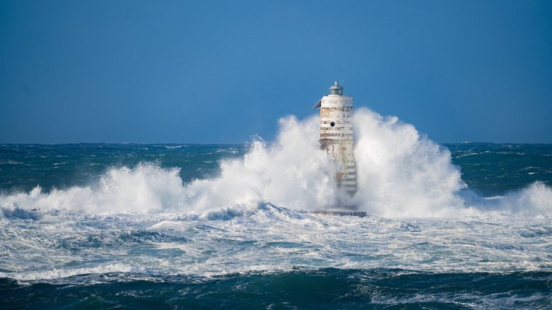 A very large wave colliding with a lighthouse.