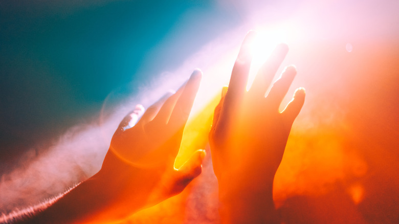 Human hands reach up into a red and orange sky