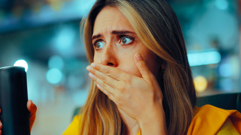 A woman holds her hand over her mouth while sitting in a restaurant and holding a drink