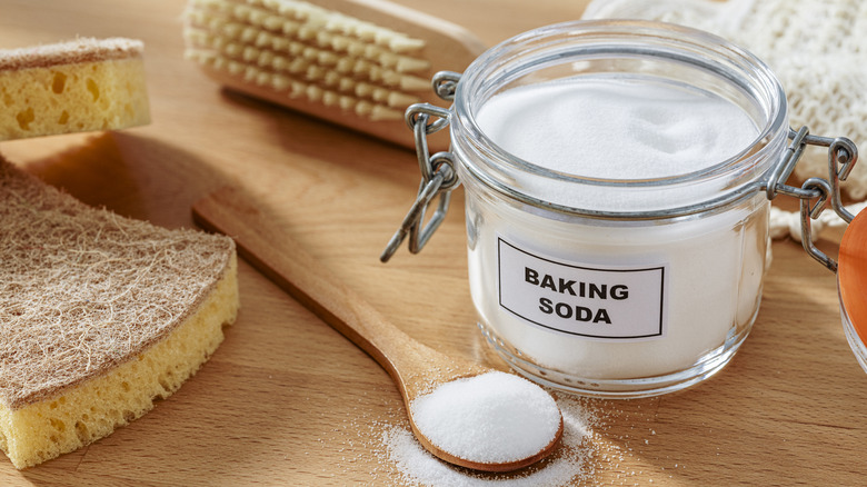 Glass jar of baking soda with wooden spoon and cleaning utensils
