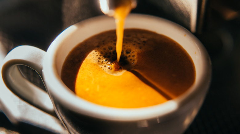 A closeup shows coffee being poured into a mug