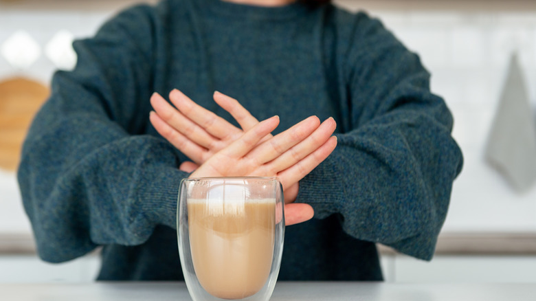 A woman crosses her hands in front of a glass of coffee