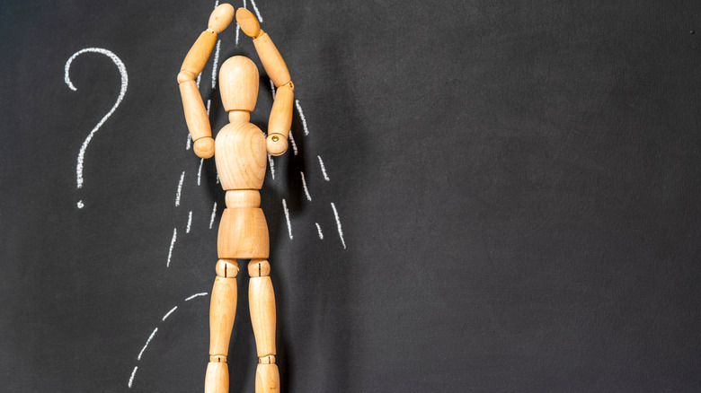 Wooden mannequin in front of a chalkboard with a question mark and drawings that make it look like the mannequin is peeing in the shower