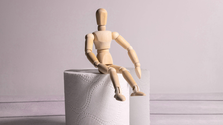A small wooden mannequin sitting on toilet paper