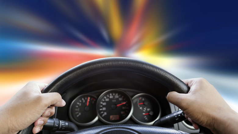Hands on a steering wheel in a car with view of blurred lights through the windshield
