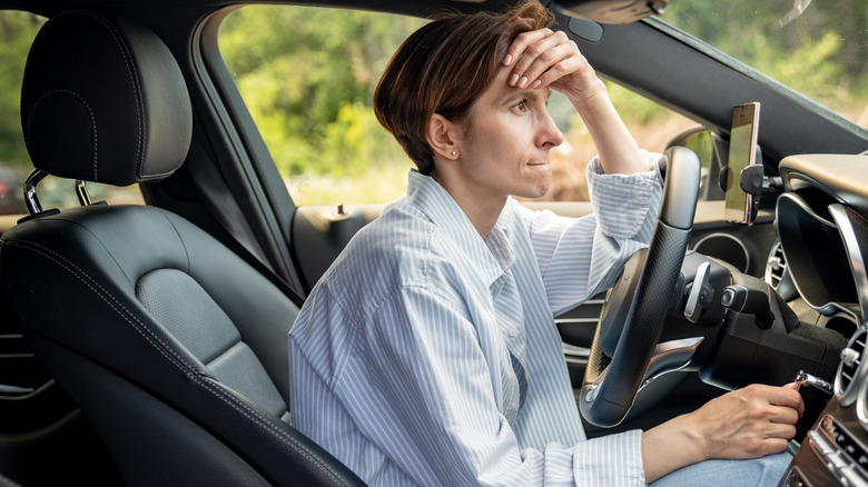 Woman in her car with her hand on her head and a look of confusion on her face