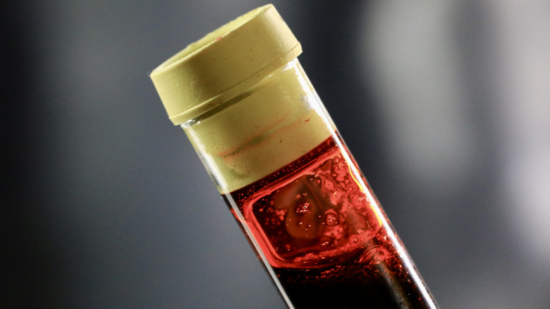 A vial of blood with a yellow cap is seen against a grey background