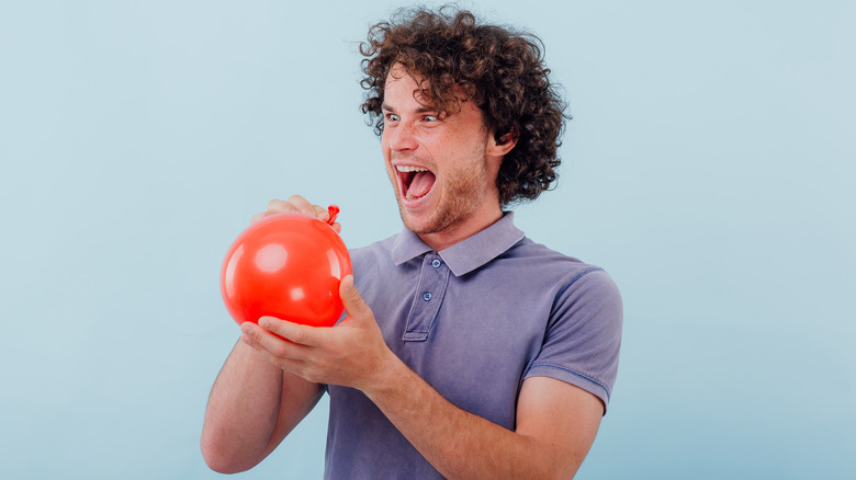 Man laughing at the sound of his voice after breathing in gas from a red balloon
