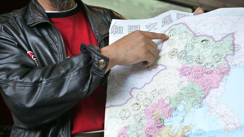 Man in leather jacket points to a northern point on a map of Manchuria