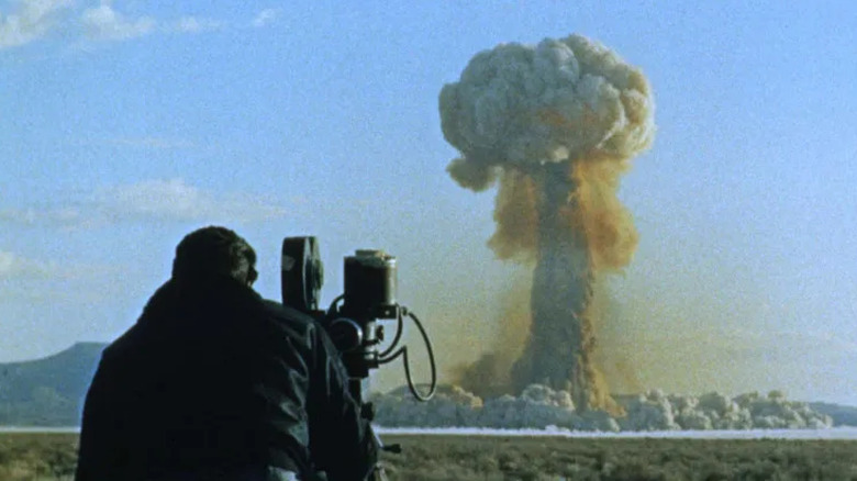 Cameraman filming atomic bomb explosion in distance, tall mushroom cloud
