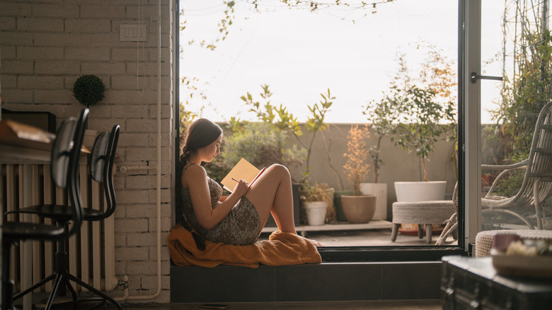 A young woman sitting in front of a window writing in a journal