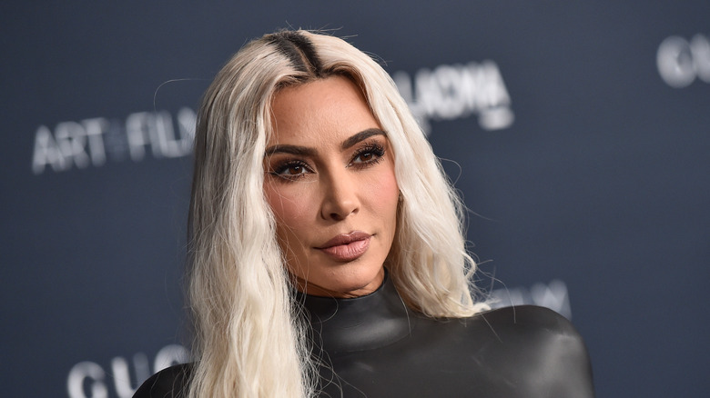 Kim Kardashian with bleached hair and skin-tight top posing at an art event