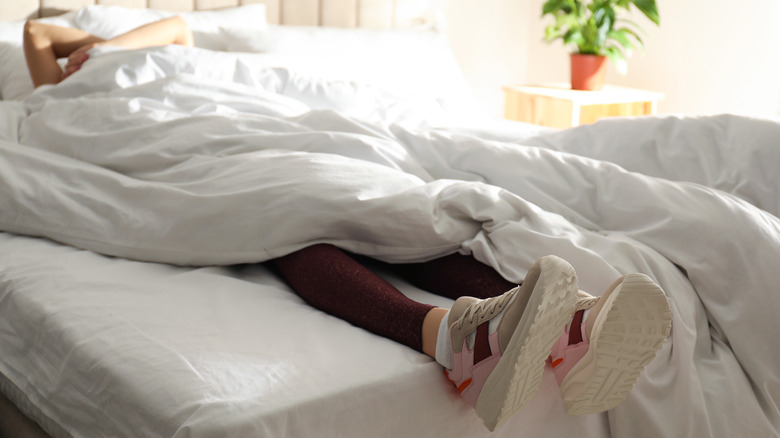 Woman under bed covers with shoes on her feet