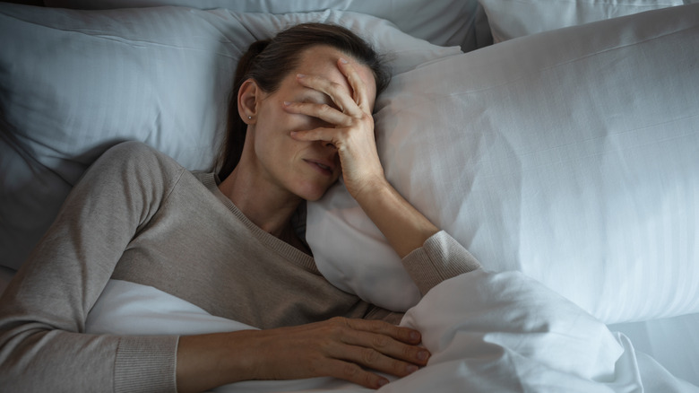 Woman in bed covering face with hand