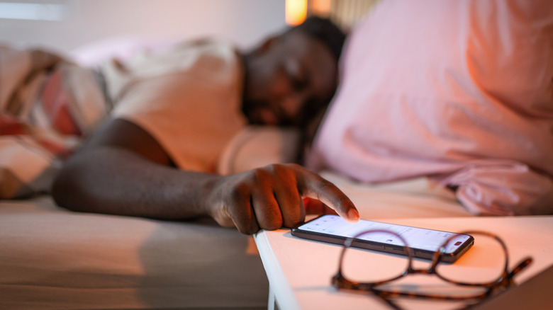 Man in bed looking at phone on nightstand