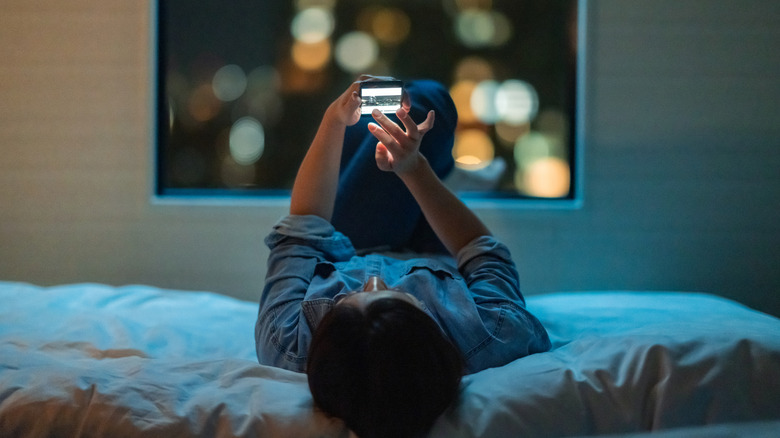 Woman looking a smartphone on bed at night