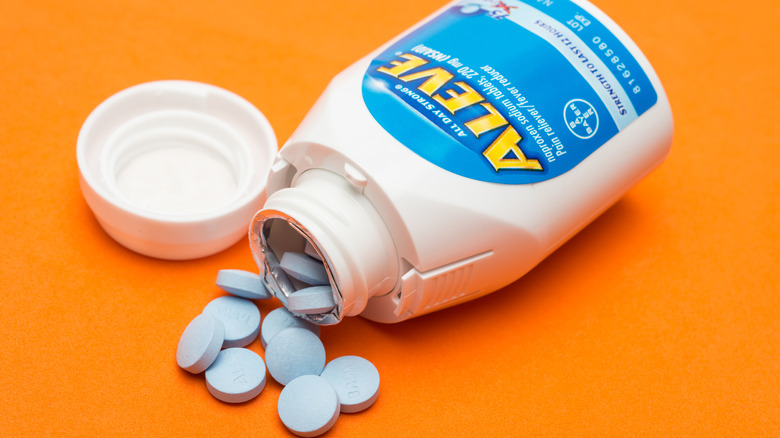 Opened bottle of Aleve on orange background