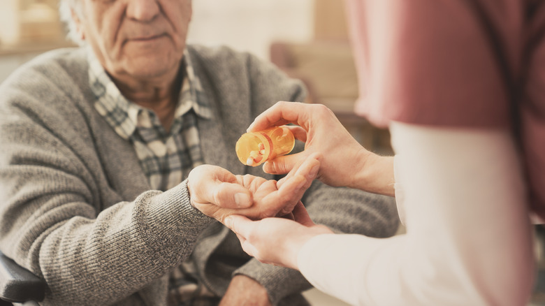 A healthcare professional hands an elderly man a pill.