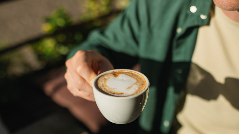 Man holding a cappuccino outdoors