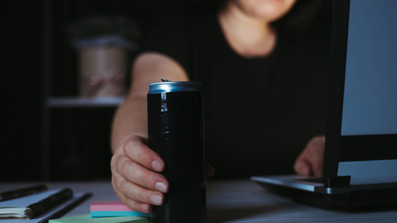 Woman reaching for energy drink can while working at night