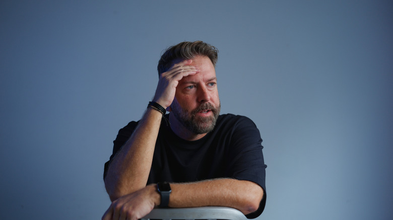 A man with a beard sits holding his head