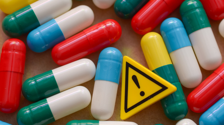 A pile of colorful capsules with a yellow triangle with an exclamation point on it indicating caution.