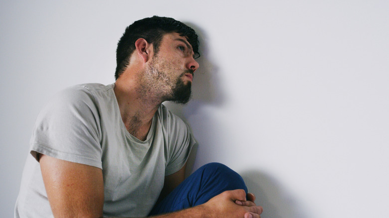 A man leaning against a wall seemingly distressed