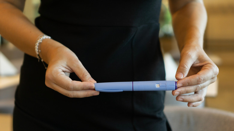 A close-up of someone in a black dress holding an Ozempic injection pen.