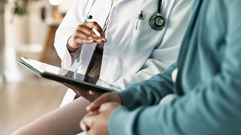 A physician holding a tablet talking to a patient.