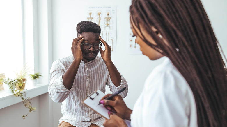 Man with hands on temples while talking with doctor