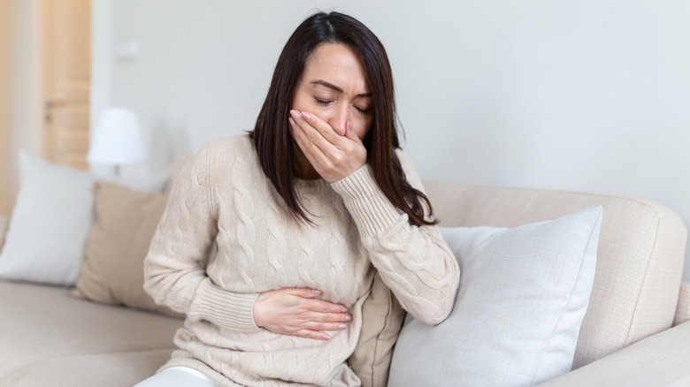 Woman sitting on sofa with hands on mouth and stomach