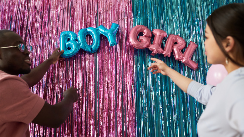Two people pointing to boy and girl balloons with tinsel in background