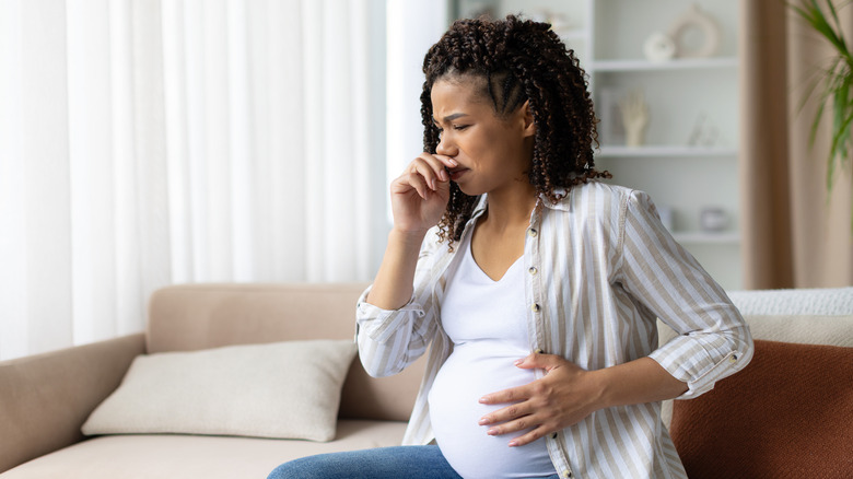 Pregnant woman fighting nausea while sitting on sofa