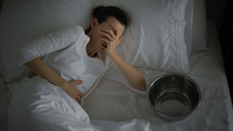 Woman lying in bed experiencing nausea with empty bowl beside her