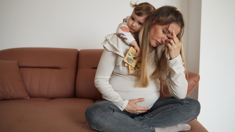 Pregnant woman experiencing discomfort while young child hugging her