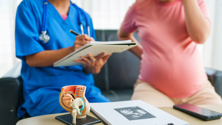 Doctor holding a clipboard while talking with a pregnant person