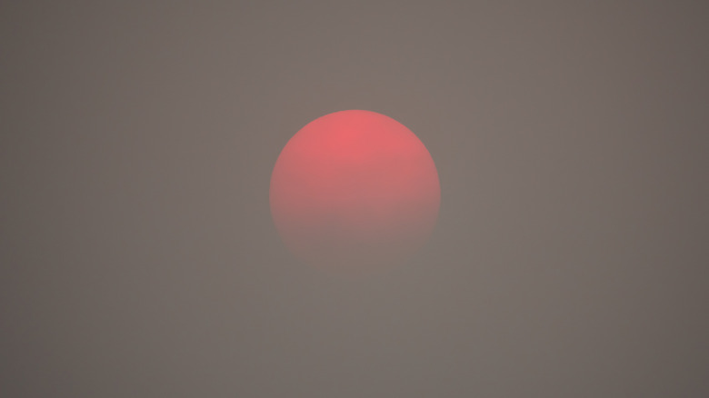 Dim red sun viewed through thick smoke in the atmosphere