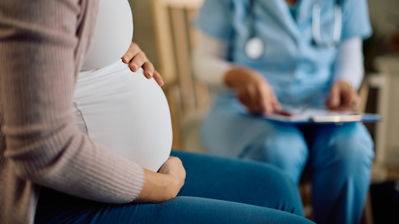 Midsection view of pregnant woman sitting with doctor