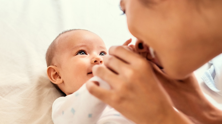 Mother smiling and holding the hands of a smiling infant
