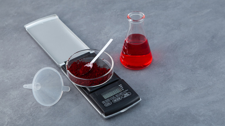 Red food dye powder on scale next to a beaker