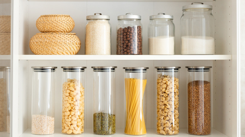 Kitchen cabinet holding glass jars of rice, pasta, and other dry goods.
