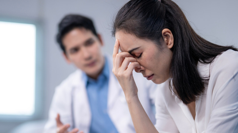 Woman sadly places hand to her face as male doctor talks