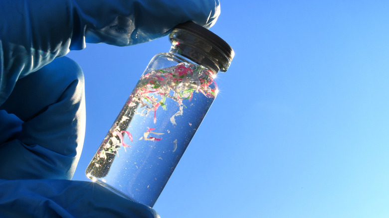 A vial of water, plastic pieces, and sand held up to the sun