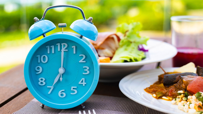 A blue alarm clock sitting next to a plate of food and in front of a salad bowl